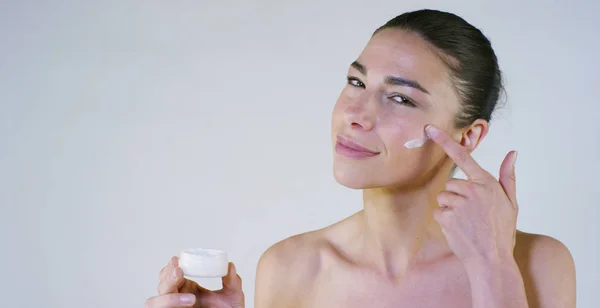 Retrato de una hermosa jovencita sonriendo y mirando a la cámara, sin maquillaje, manchando la cara de crema, sobre un fondo blanco.Concepto: belleza natural, juventud, cuidado de la piel, siempre joven, ámate . —  Fotos de Stock