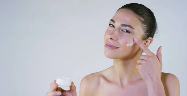 Retrato de una hermosa jovencita sonriendo y mirando a la cámara, sin maquillaje, manchando la cara de crema, sobre un fondo blanco.Concepto: belleza natural, juventud, cuidado de la piel, siempre joven, ámate . —  Fotos de Stock