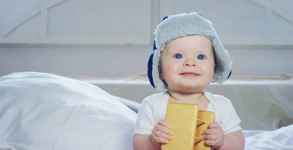 Um bebê, um menino com grandes olhos azuis e cabelos claros, senta-se e sorri em um cobertor branco de neve, olha para sua mãe, em um fundo branco . — Fotografia de Stock
