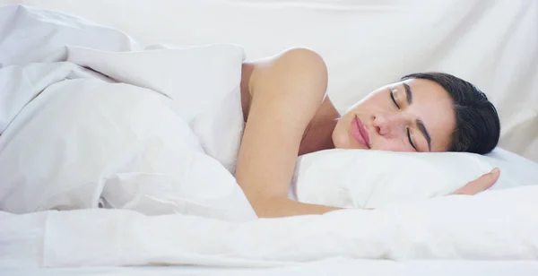 A simple working day for a beautiful young girl sleeping in a warm bed, covered with a soft warm white blanket, on a white background. — Stock Photo, Image