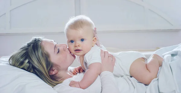 Os melhores momentos da vida, uma jovem mãe amorosa e feliz abraça um filho de enfermagem, em um cobertor branco de neve, em um fundo branco. conceito de amor, família e felicidade — Fotografia de Stock