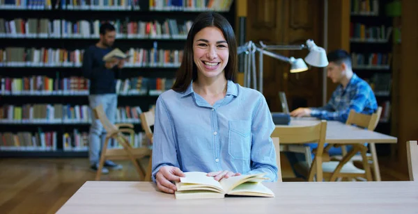 Retrato de uma bela jovem sorrindo feliz em uma biblioteca segurando livros depois de fazer uma pesquisa e depois de estudar. Conceito: educativo, retrato, biblioteca e estudioso . — Fotografia de Stock