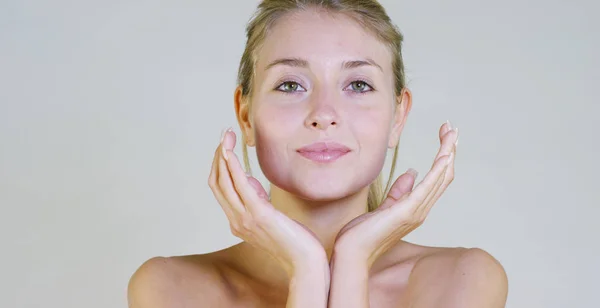 Portrait of a beautiful young girl smiling and looking at the camera, without makeup, after cream, on a white background. Concept: natural beauty, youth, skin care, always young, to love yourself. Stock Photo