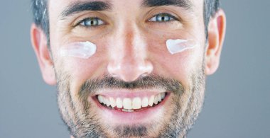 Çok yakışıklı bir adam gülümsüyor ve anti-kırışıklık ve anti-aging vücut bakımı için yüz kremi ve göz kontur koyar ve güzellik bilir. Konsept: Güzellik, krem, güzellik