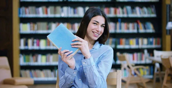 Μια όμορφη νεαρή γυναίκα που σπουδάζουν σε μια ευτυχισμένη και ανέμελη βιβλιοθήκη ανάγνωση του βιβλίου. Έννοια: εκπαιδευτικό, πορτραίτο, βιβλιοθήκη, και φιλομαθής, να χαλαρώσετε. — Φωτογραφία Αρχείου
