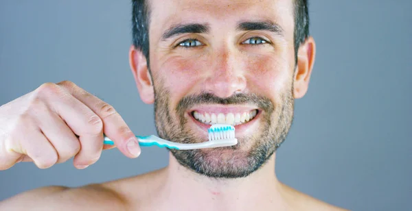 Ett vackert porträtt av man ler och lyser hans vita tänder visar hans tandborste och dentrifricio för tappade tänder rekommenderas av sin tandläkare. Koncept: skönhet, tandläkare, munhygien — Stockfoto