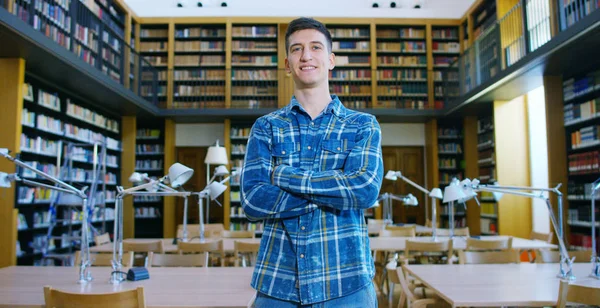 Ritratto di un bel ragazzo sorridente felice in una biblioteca che tiene libri dopo aver fatto una ricerca e dopo aver studiato. Concetto: educativo, ritratto, biblioteca e studioso . — Foto Stock