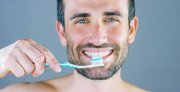 Ett vackert porträtt av man ler och lyser hans vita tänder visar hans tandborste och dentrifricio för tappade tänder rekommenderas av sin tandläkare. Koncept: skönhet, tandläkare, munhygien — Stockfoto