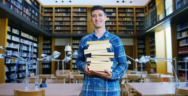 Portréja egy gyönyörű fiatal fiú mosolyogva boldog gazdaság könyvek csinálás egy kutatás és tanulás után a könyvtárban. Koncepció: oktatási, portré, könyvtár, és szorgalmas. — Stock Fotó
