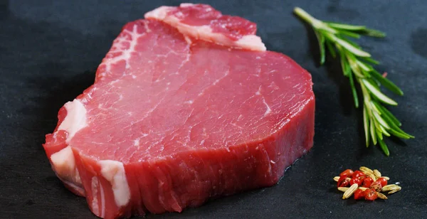 Belo bife suculento de carne fresca em uma mesa com sal, alecrim, alho e tomate em um fundo preto, vista superior. Conceito: produtos frescos e naturais, produtos biológicos, produtos à base de carne, orgânicos, nutrição . — Fotografia de Stock