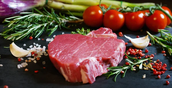Beautiful juicy fresh meat steak on a table with salt, rosemary, garlic, and tomato on a black background, top view. Concept: fresh & natural products, bio products, meat products, organic, nutrition. — Stock Photo, Image