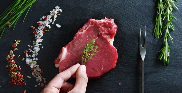 Steak daging segar yang lezat di atas meja dengan garam, rosemary, bawang putih, dan tomat di latar belakang hitam, pemandangan atas. Konsep: produk segar & alami, produk bio, produk daging, organik, nutrisi . — Stok Foto