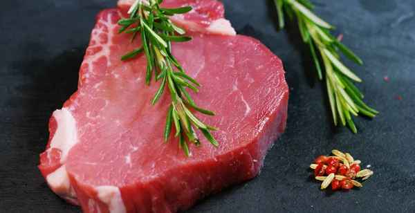 Schöne saftige Steak mit frischem Fleisch auf einem Tisch mit Salz, Rosmarin, Knoblauch und Tomaten auf schwarzem Hintergrund, Draufsicht. Konzept: Frische & Naturprodukte, Bioprodukte, Fleischprodukte, Bio, Ernährung. — Stockfoto