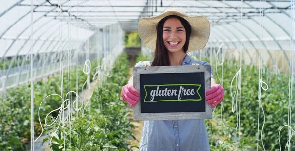 En vacker flicka i en stråhatt och bär Rosa gummihandskar, innehar en svarta tavlan, i ett växthus. Koncept: bioprodukter, naturliga produkter, färska, läckra, frukter, grönsaker, växa, vatten, växter — Stockfoto