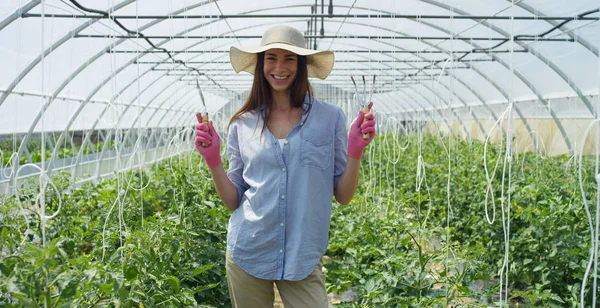 Portret piękna dziewczyna w słomkowym kapeluszu i noszenia rękawic gumowych różowy, uśmiechnięty, w szklarni. Koncepcja: bio produkty, produkty naturalne, świeże, pyszne, owoce, warzywa, rosnąć, woda, rośliny. — Zdjęcie stockowe