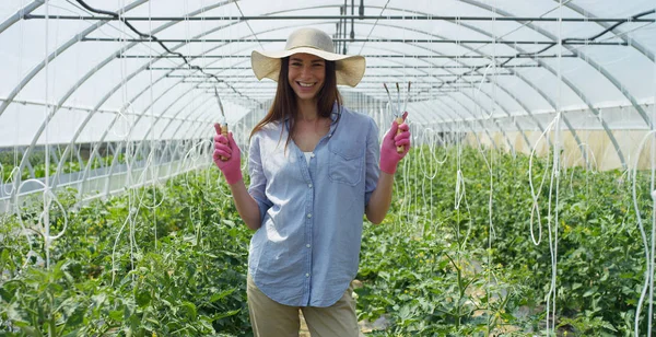 Retrato Menina bonita em um chapéu de palha e usando luvas de borracha rosa, sorrindo, em uma estufa. Conceito: produtos biológicos, produtos naturais, frescos, deliciosos, frutas, legumes, crescer, água, plantas . — Fotografia de Stock