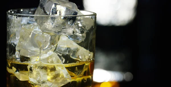Whisky versé dans un verre avec de la glace, au ralenti, prise de vue macro, sur une table en bois et fond sombre. Concept : alcool, spiritueux, pour une bonne soirée, l'alcool nuit à la santé. — Photo