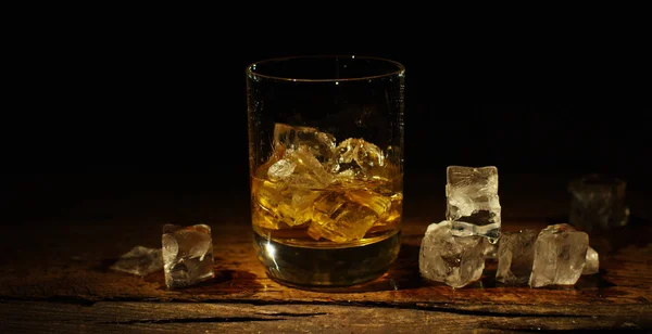 Whiskey poured into a glass with ice, in slow motion, macro shooting, on a wooden table and dark background. Concept: alcohol, spirits, for a good evening, alcohol harms health.