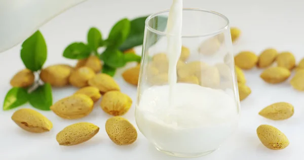 La leche de almendras se vierte en un vaso en cámara lenta, el fondo en los bosques hay almendras, perfecto para una dieta para una dieta saludable y se puede utilizar como medicina. concepto: dieta, aptitud, medicina . —  Fotos de Stock