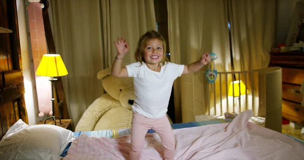 明るく、幸せな小さな女の子は、両親のベッドを再生する上でジャンプします。幸せな子。若さ、喜びと幼年期の幸福の概念。安全な家と保護の概念. — ストック写真