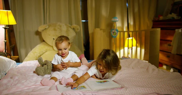 Gadis kecil yang ceria dan bahagia membaca di tempat tidur orang tua mereka untuk bermain. Anak yang bahagia. konsep pemuda, sukacita dan kebahagiaan di masa kanak-kanak. konsep rumah aman dan perlindungan . — Stok Foto