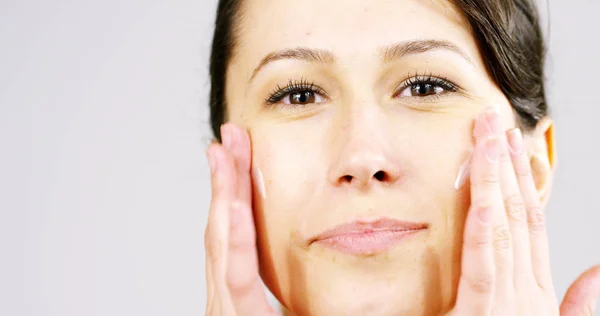 Le portrait d'une jeune femme à la peau parfaite appliquant une crème jour / nuit sur son visage préalablement nettoyé. Concept de soins de la peau, cosmétiques, beauté, centre de bien-être, soins du visage, massage facial — Photo