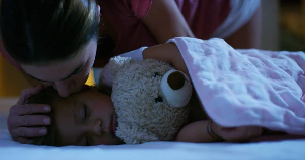 Ibu yang baik memberikan ciuman depan untuk bayinya sebelum tidur dan menutupinya dengan sangat manis dengan selimut merah muda dan biru pada bahan wol, konsep hangat dan perawatan kesehatan — Stok Foto