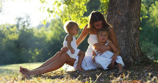Mother with little girls dressed in a vintage lawn round dence close to a tree in sunset happy little girl in nature. concept of nature and sustainability, connection with nature and the green world. — Stock Photo, Image