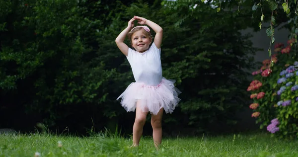 Malá holčička se snaží učinit první kroky tanečnice v zahradě, oblečený jako trochu legrační šťastný tanečnice tanečník. koncept první kroky a přírody šťastné dětství. vtipné děti. Cinema camera — Stock fotografie