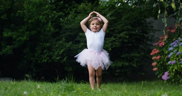 Kislány próbál lépéseket tesznek az első táncos öltözött, mint egy kis táncos boldog táncos vicces kertben. koncepció első lépések és a természet boldog gyermekkor. kicsit vicces gyerekek. fényképezőgép mozi — Stock Fotó