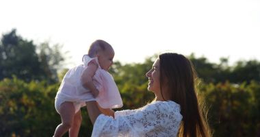 Süper ağır çekim bir güneşli bir günde 4 k onun bebek kız e bağ çayırda dönen genç beyaz anne (yakın fişekleri ile)