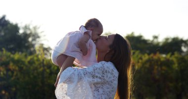 Süper ağır çekim bir şefkatle 4 k bir güneş bağında bir çayırda onun bebek kız öpüşme genç beyaz anne (yakın fişekleri ile)