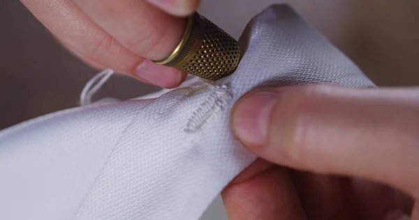 Een hand van een jonge naaister naaien een witte doek tailoring volgens de traditie van kleermakers. De naaister gebruik perfect naald en draad naaien traditionele concept, naaien, stijl en mode — Stockfoto