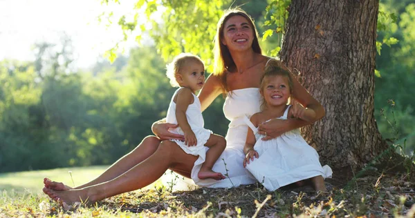 Madre con niñas vestidas en un césped vintage sentado cerca de un árbol en la puesta del sol niña feliz en la naturaleza. concepto de naturaleza y sostenibilidad, conexión con la naturaleza y el mundo verde . —  Fotos de Stock