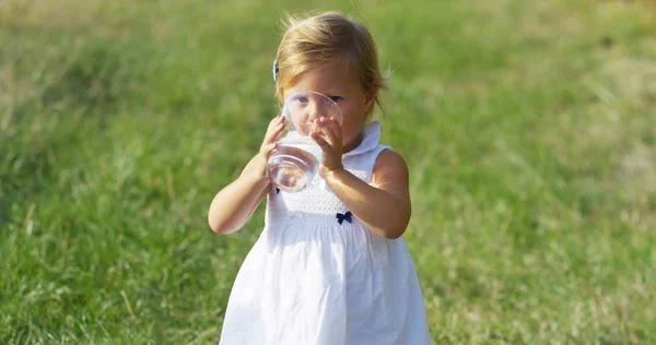 Gadis kecil yang cantik berusia 2 tahun minum segelas air bersih gadis kecil di kebun anggur di alam minum segelas air jernih dan murni seperti masa mudanya. konsep kemurnian dan air bersih — Stok Foto