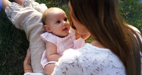 Super slow motion of young caucasian mother kissing tenderly her baby girl in a meadow of vineyard on a sunshine in 4k (close up with flares)