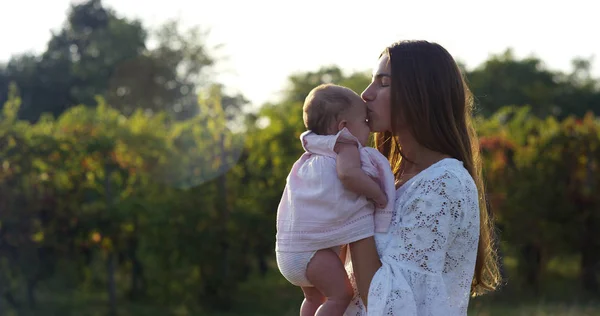 Супер замедленная съемка молодой кавказской мамаши, нежно целующей свою малышку на лугу виноградника на солнышке в 4К (крупным пламенем ) — стоковое фото