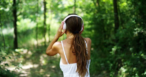 Una mujer en el verde con auriculares escuchando música, cantando, bailando y divirtiéndose con un aire despreocupado. La música le da la energía para cantar y ser feliz. la música hace volar la imaginación — Foto de Stock