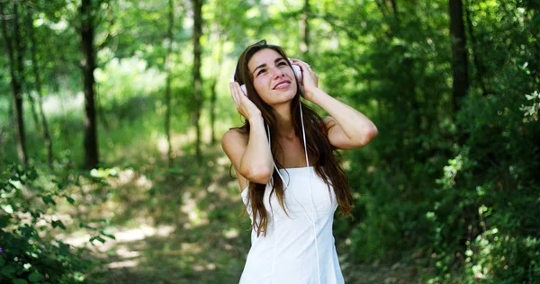Une femme dans le vert portant des écouteurs écoutant de la musique, chantant, dansant et s'amusant avec un air insouciant. La musique lui donne l'énergie de chanter et d'être heureux. la musique fait voler l'imagination — Photo