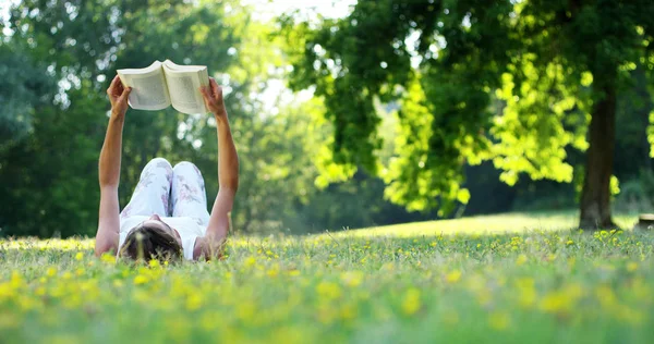 On a sunny day a beautiful woman relaxes in the shade of a tree to read a book and relax, the book really like the woman who is a lover of literature and silence. relax — Stock Photo, Image