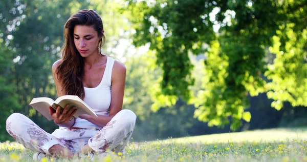 В солнечный день красивая женщина расслабляется в тени дерева, чтобы почитать книгу и расслабиться, книга действительно нравится женщине, которая является любителем литературы и тишины. расслабиться — стоковое фото