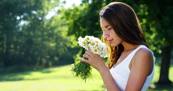 Una mujer rodeada de vegetación ha recogido flores y las cuenta en pensamiento, pensando en su amor piensa en su vida que pasa. flores que traen recuerdos de los buenos recuerdos . — Foto de Stock