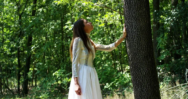 En un día soleado una mujer abrazando el árbol como un signo de amor por la naturaleza. Naturaleza que ama y protege porque el árbol es un símbolo de la vida. La mujer naturalista es despreocupada y sonriente — Foto de Stock