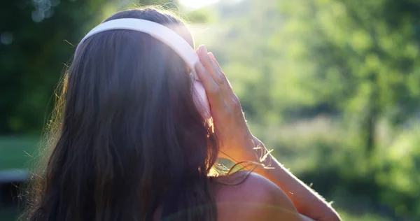 Una mujer en el verde con auriculares escuchando música, cantando, bailando y divirtiéndose con un aire despreocupado. La música le da la energía para cantar y ser feliz. la música hace volar la imaginación — Foto de Stock