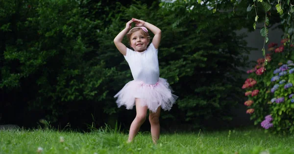 An einem sonnigen Frühlingstag dreht sich ein kleines Mädchen wie eine Balletttänzerin im Garten herum und lächelt glücklich — Stockfoto