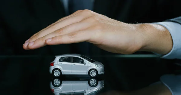 Un hombre vestido con traje y corbata, muestra un pequeño auto. Concepto: seguro de coche, mecánico, arrendamiento, compra de coches nuevos y usados y garajes públicos . — Foto de Stock