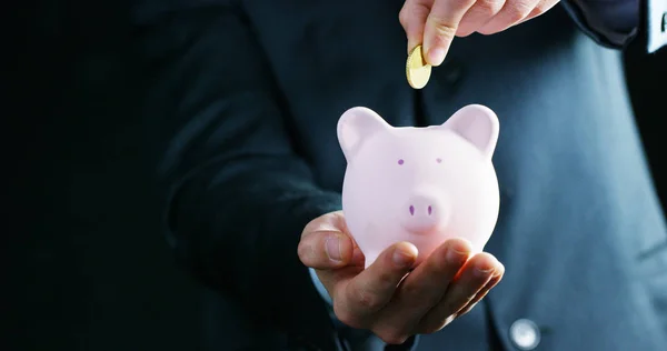 A man dressed in a suit and tie, puts money into the piggy bank. Concept: Pension, savings, investment, accumulation plan, savings for college studies. — Stock Photo, Image