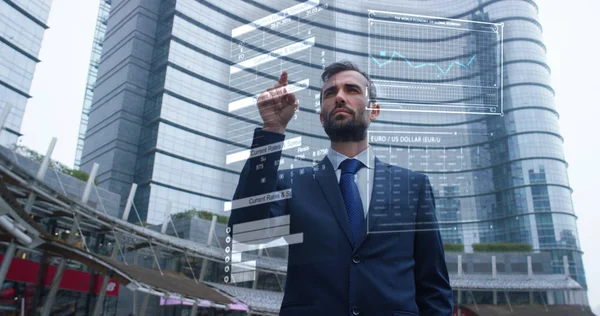 A businessman in a suit uses holography and augmented reality to see in 3D graphics financial economics in his office in a skyscraper. — Stock Photo, Image