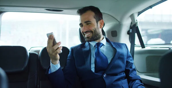 Ένας επιχειρηματίας ενώ ταξιδεύετε με αυτοκίνητο στο πίσω κάθισμα, οικογενειακά βίντεο κλήσεις με το κινητό σας τηλέφωνο. Ο άνθρωπος στην καριέρα οδηγού για τα επαγγελματικά του ταξίδια. Έννοια των επιχειρήσεων μεταφορών, πλούτο, τεχνολογία — Φωτογραφία Αρχείου