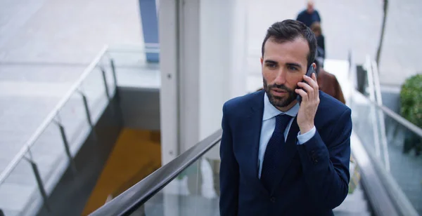 Em escadas rolantes, um homem de negócios atende o telefone, envia mensagens e sorri para a bela notícia de trabalho. Conceito: tecnologia, telefonia, viagens de negócios, negócios . — Fotografia de Stock